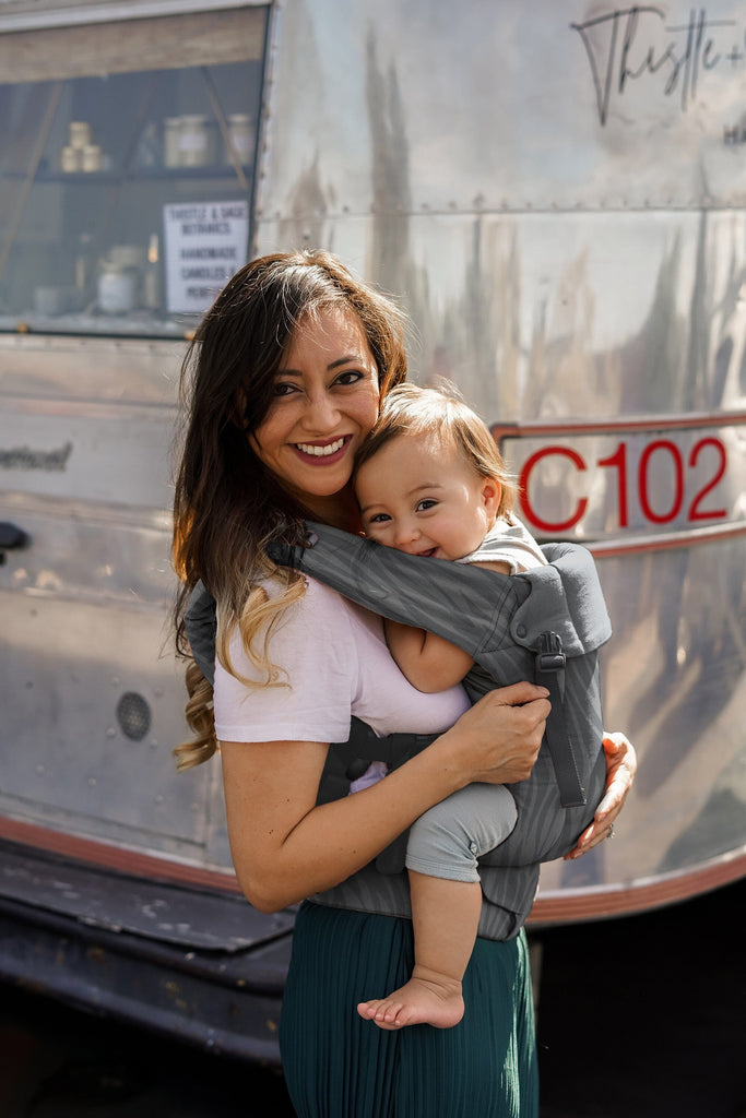 Baby in the Beco Gemini Baby Carrier in Dark Zebra pattern, front carry position shown.