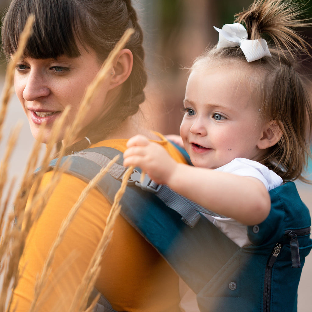 Beco 8 carrier in teal with a baby in back carry position