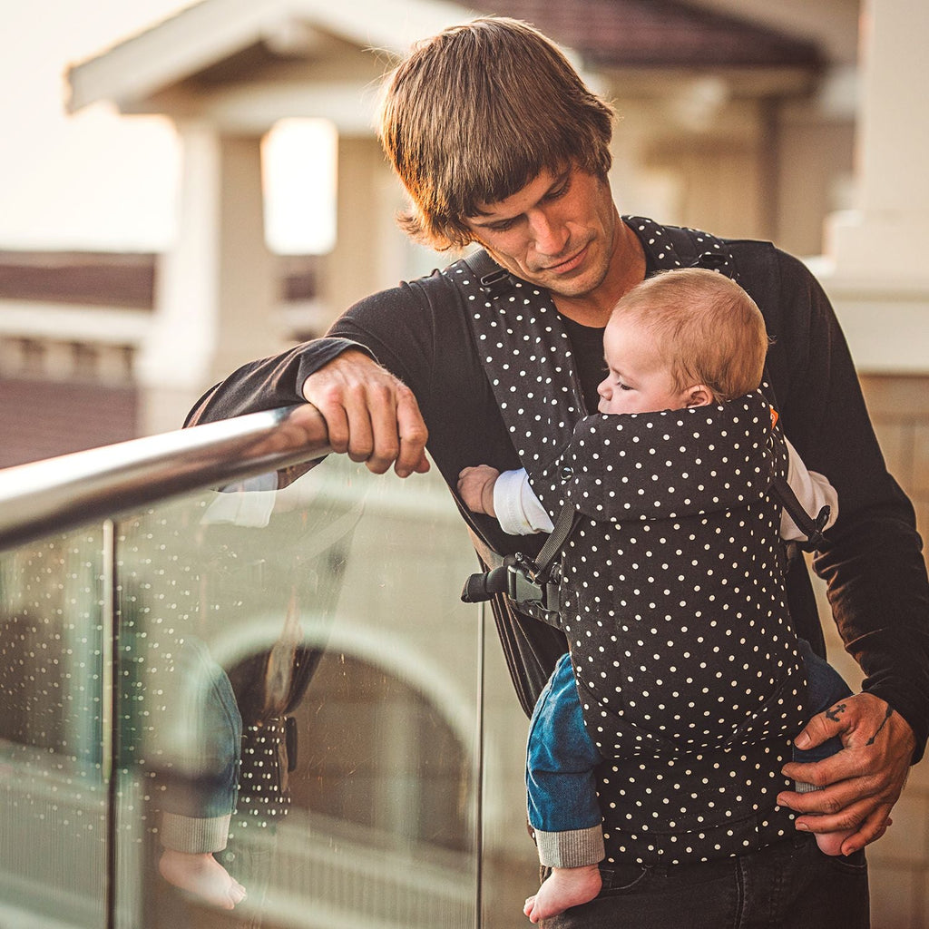 Baby in front carry facing in position in a Beco Gemini baby carrier in black with white polka dots