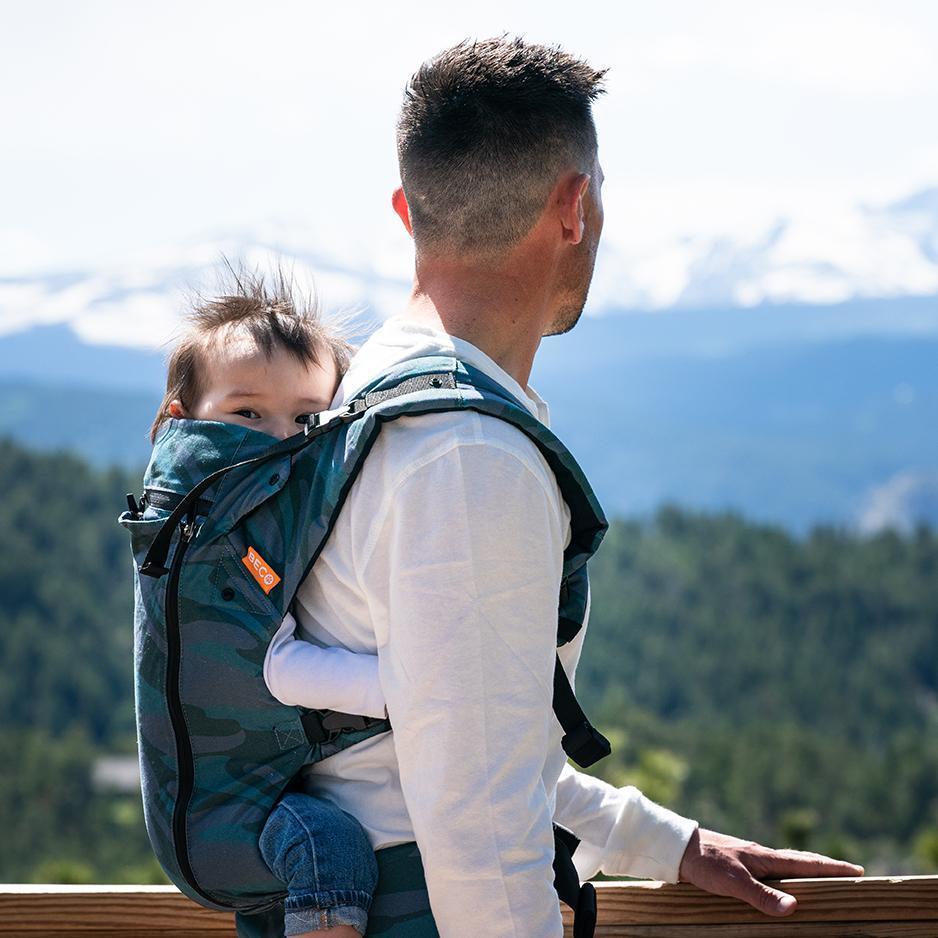 Parent wearing blue toned camo print Beco 8 carrier with child in back carry position