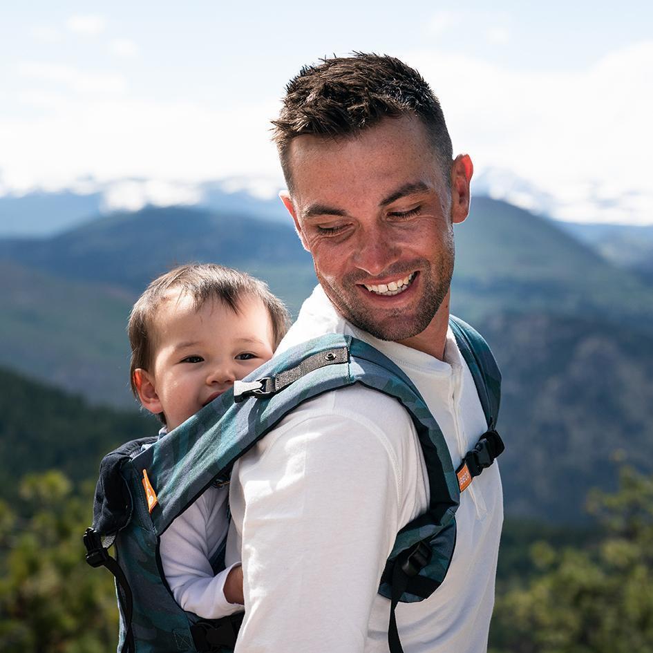 Parent wearing blue toned camo print Beco 8 carrier with child in back carry position