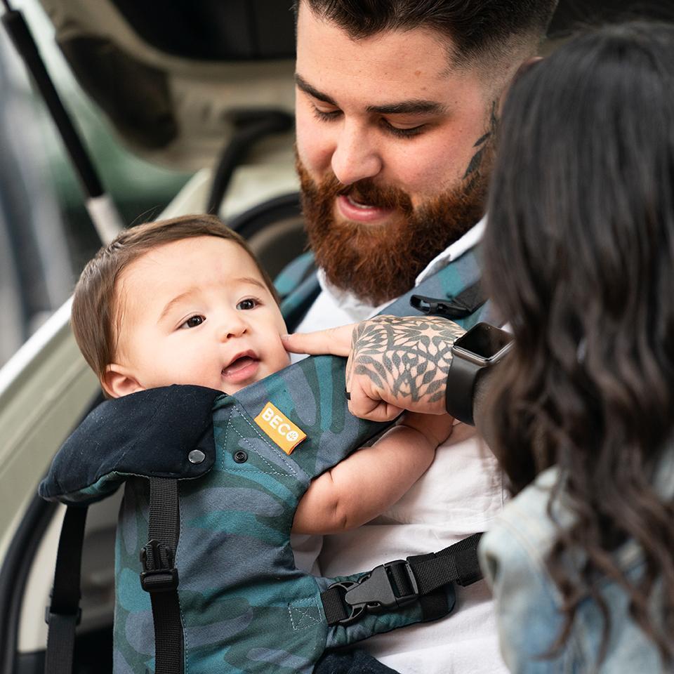 Parent wearing blue toned camo print Beco 8 carrier with child in front carry facing in position