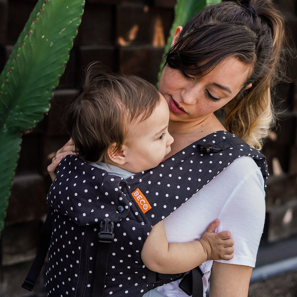 Baby in front carry facing in position in a Beco 8 baby carrier in black with white polka dots