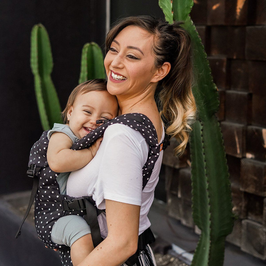 Baby in front carry facing in position in a Beco 8 baby carrier in black with white polka dots